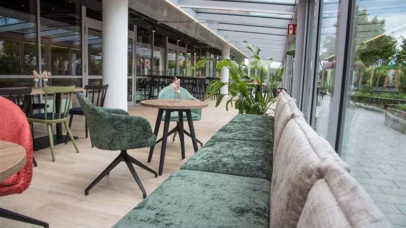 Innenansicht einer modernen Kantine mit Sitzplätzen am Fenster, Tischen, Stühlen und Pflanzen.