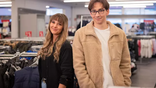 Zwei Mitarbeitende stehen nebeneinander in einer modernen Filiale und lächeln