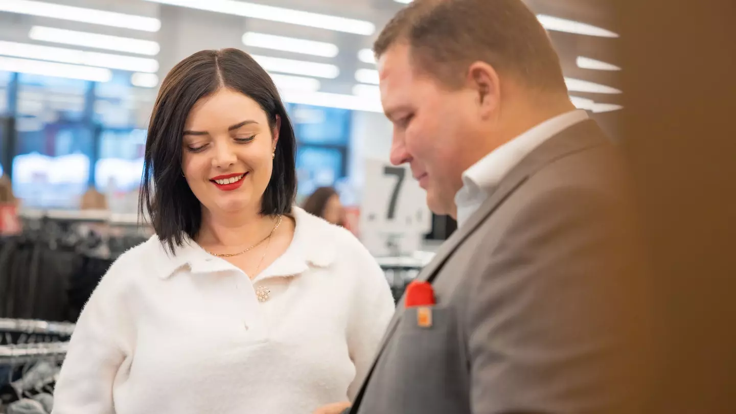 Zwei Mitarbeitende schauen lächelnd auf einen Gegenstand hinab in der Filiale