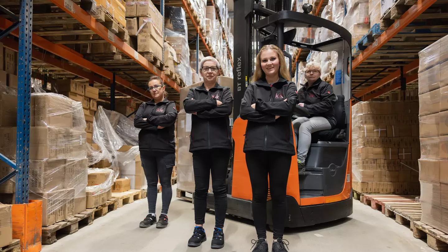 Drei Mitarbeitende stehen im Lager mit verschrenkten Armen und schauen in die Kamera, ein Mitarbeinder sitzt auf einem Gabelstabler und schaut ebenfalls in die Kamera