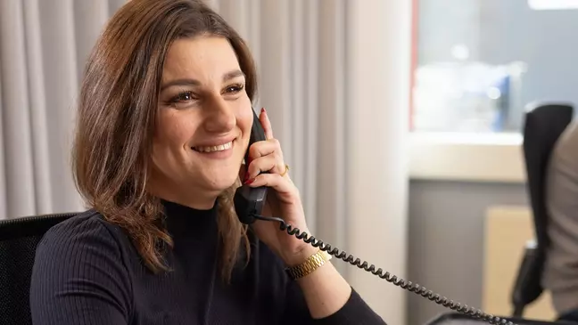 Eine Frau telefoniert während sie am Arbeitsplatz sitzt und lächelt