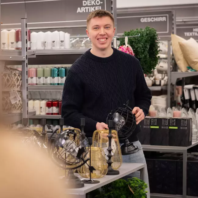 Ein Mitarbeiter steht lächelnd in einer modernen Filiale und präsentiert Ware