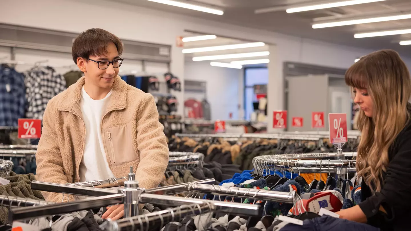 Zwei Mitarbeitende schauen sich Kleidungsstücke in einer modernen Filiale an und lächeln