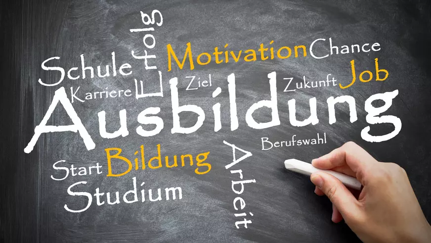 auf einer schwarzen Tafel hat eine Hand groß das Wort "Ausbildung" mit Kreide geschrieben und weitere Worte