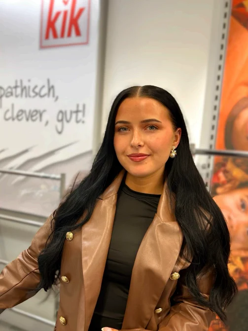 Abgebildet ist eine stehende Frau mit langen dunklen Haaren.