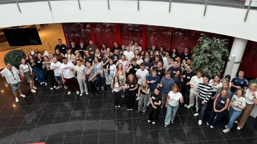Eine Gruppe von vielen Menschen steht in einem Foyer und schaut nach oben zum Fotoapparat.