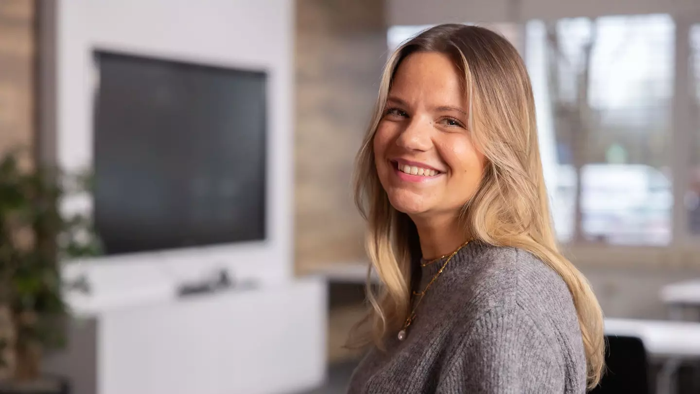 Eine Frau schaut lächelnd in die Kamera, sie steht in einer modernen Räumlichkeit