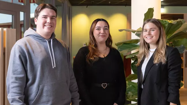 Drei Mitarbeitende stehen in einer modernen Räumlichkeit und lächeln