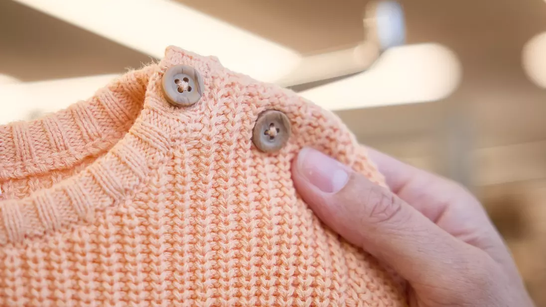Eine Hand hält einen orangen Kinderpulli mit Knöpfen am Ausschnitt