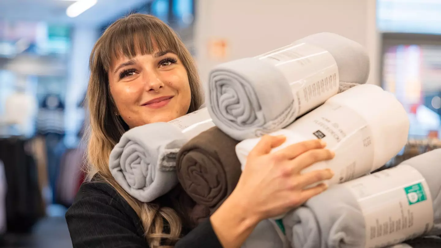 Eine Frau steht lächelnd in einer Filiale und hält viel Ware in den Händen