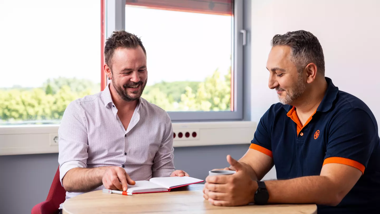 Zwei Männer sitzen an einem Tisch und sprechen in freundlicher Atmosphäre miteinander.