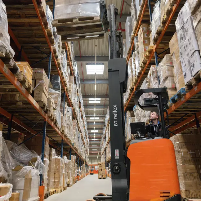 Ein Lagermitarbeiter bedient einen Hochregalstapler in einem Hochregallager und lagert Ware ein