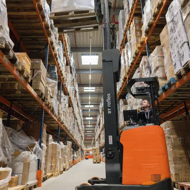 Ein Lagermitarbeiter bedient einen Hochregalstapler in einem Hochregallager und lagert Ware ein