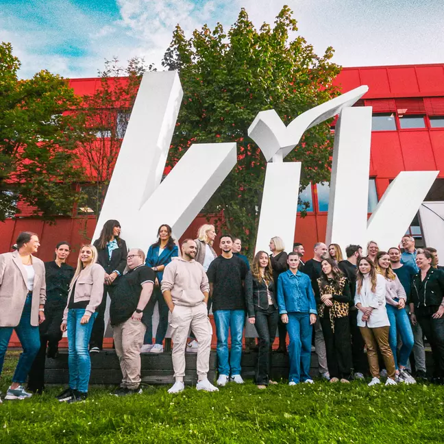 Mitarbeitende posieren vor der Europazentrale in Bönen vor einem großen KiK-Logo für ein Gruppenfoto