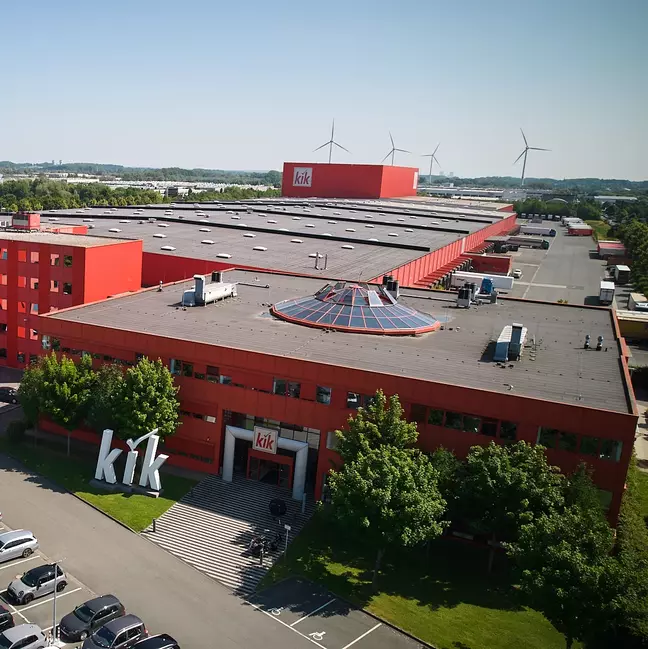 Ein großes, rotes Firmengebäude mit dem Logo „kik“ steht in einer grünen Landschaft.