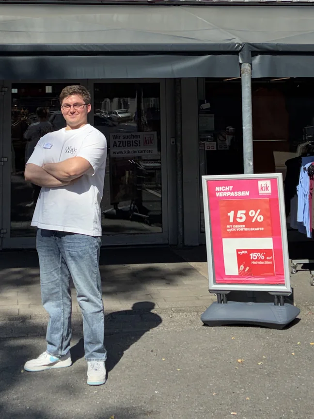 Ein lächelnder Mann mit Brille steht vor einer Fensterfront mit verschänkten Armen.
