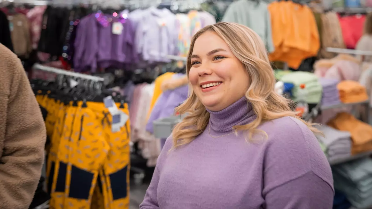 Eine Frau ist umgeben von Kleidungsstücken in einem Raum