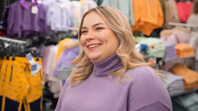 Eine Frau ist umgeben von Kleidungsstücken in einem Raum