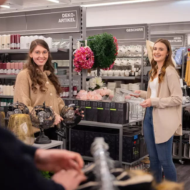 Zwei Mitarbeiterinnen stehen in einer Filiale und präsentieren Ware mit einem Lächeln im Gesicht
