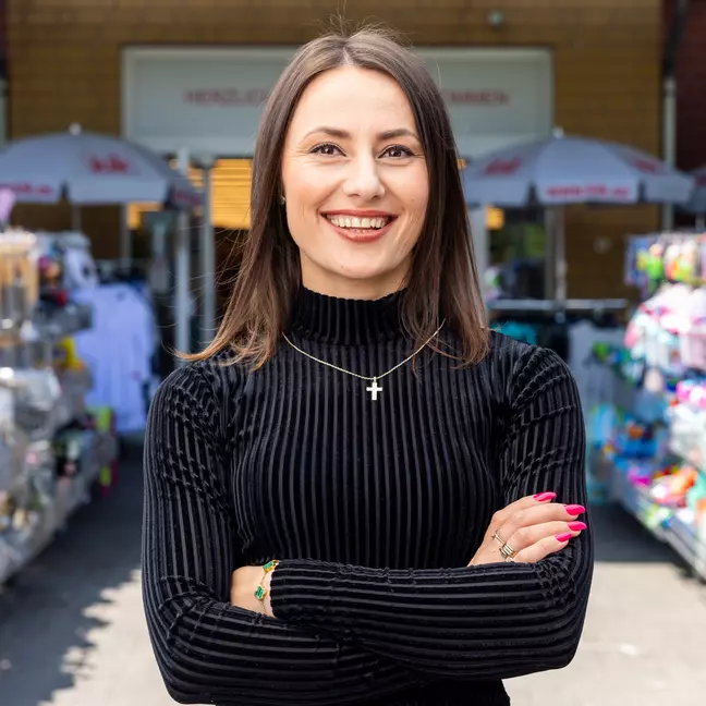 Eine Person steht im Außenbereich vor der Filiale zwischen Warenständern und blickt lächelnd in die Kamera.