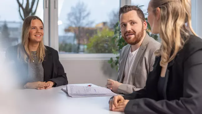 Drei Personen sitzen bei einem Bewerbungsgespräch in einem modernen Büro