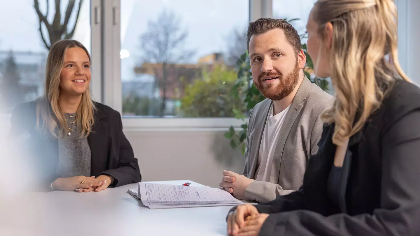 Drei Personen sitzen bei einem Bewerbungsgespräch in einem modernen Büro
