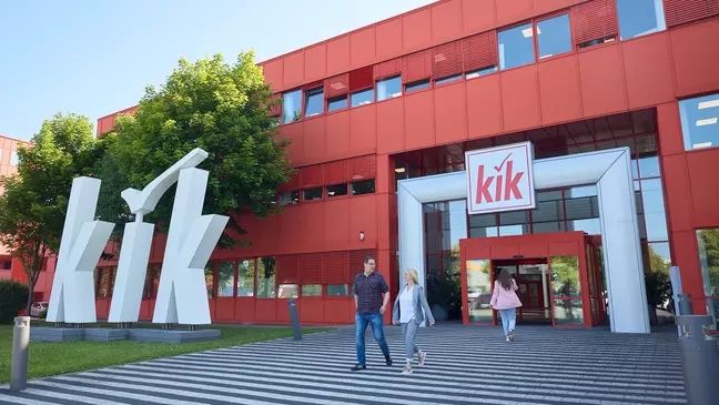 Rotes KiK-Gebäude mit großem weißen Logo vor dem Eingang und mehrere Personen auf dem Weg ins Gebäude.