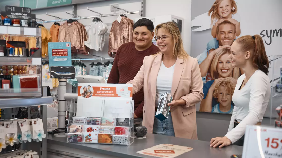 Drei Personen stehen gemeinsam an einem Verkaufstresen in einer Filiale und schauen auf die Kasse.