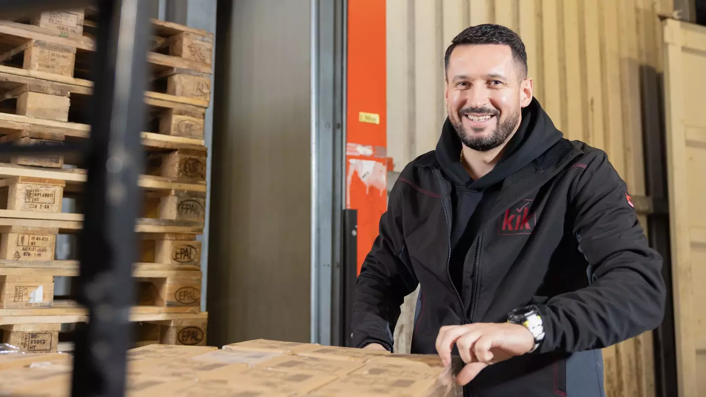 Ein Mitarbeiter steht in einem Lager und packt lächelnd Lagerware aus